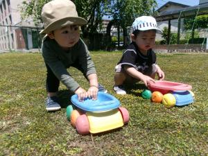 園庭でおもちゃの車を走らせる1歳児二人。