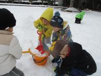 友だちと一緒にバケツに雪を集める2歳児
